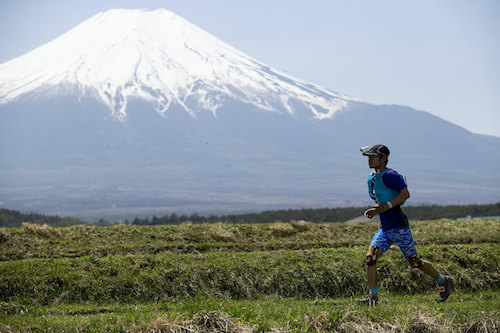 The World Trail Majors. A man is running in front of the camera with Mount Fuji in the distance behind him, covered with snow