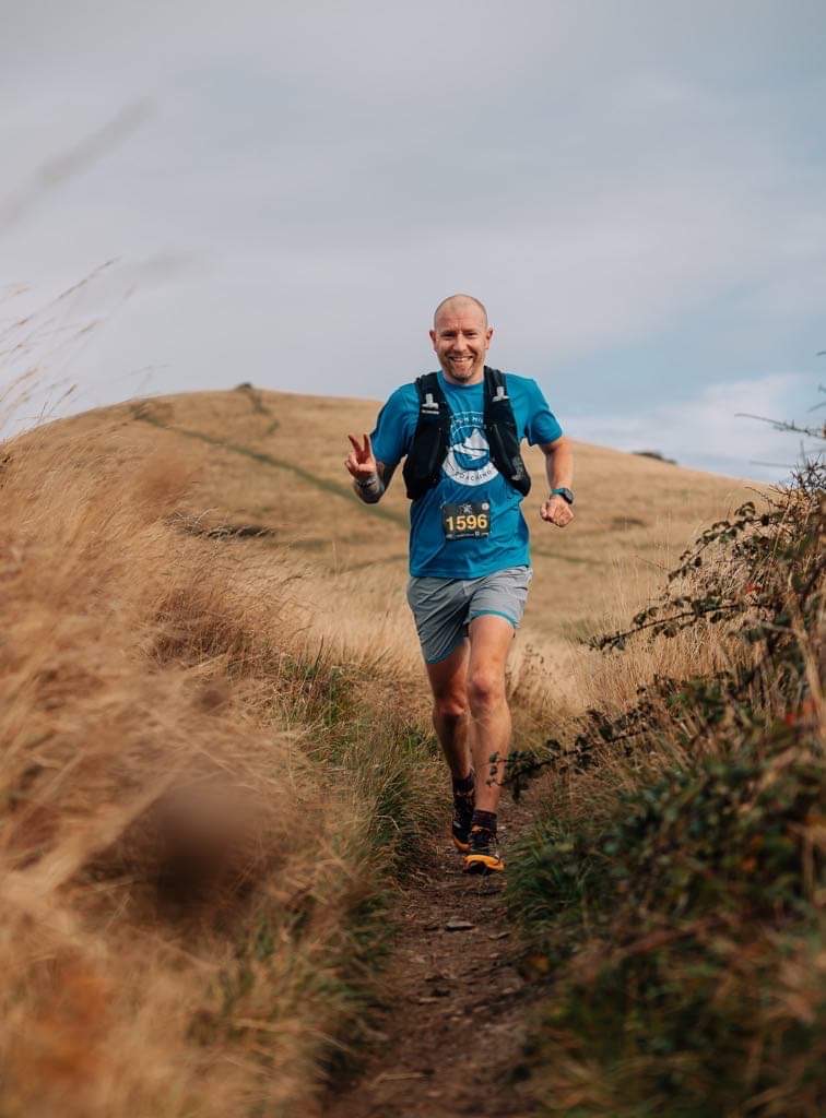 Delving into the world of strength training for ultra runners - a man running down a track in the middle of a field towards the camera during a race