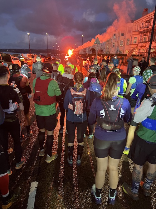 Running into Trouble: a group of people standing in the dark on a start line of a race with a red flare lighting up the scene