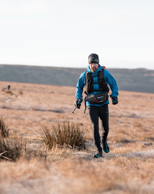 THE WINTER SPINE 2024 - Sam Hill walking across moorland dressed for cold weather and carrying poles