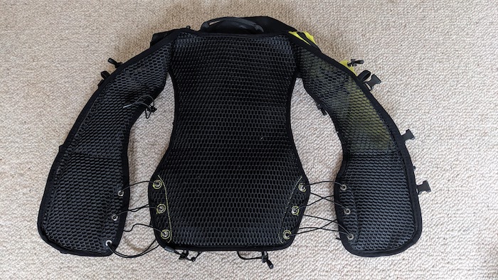 Instinct XX20-24 Trail Running Vest. The vest is laid out on a carpet, showing the inside. It is a black and soft pile material with black straps where you can adjust the fit.