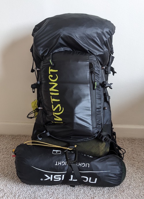 The Instinct XX20-24 Trail Running Vest is standing on the floor, packed and ready to go. You can see the water resistant material with the yellow Instinct lettering across the back.