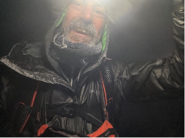 Bill wearing a black jacket and a head torch, at night, showing frost on his beard 
