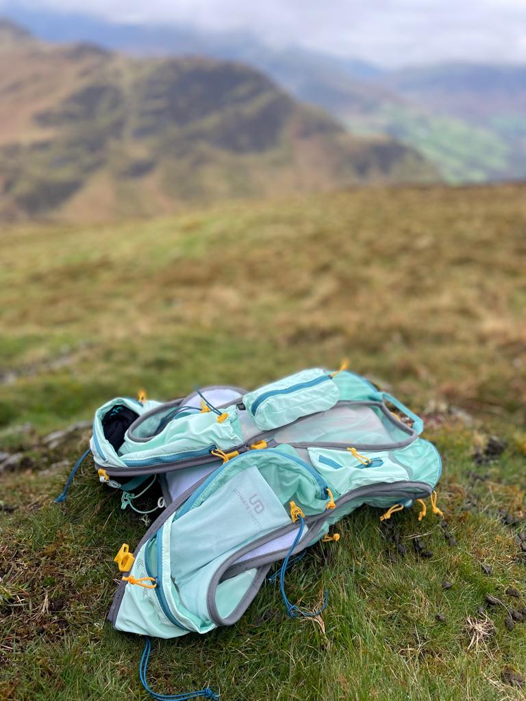 Ultimate Direction Adventure Vest/Vesta 6.0 RunUltra Review A blue vest lying on a hillside top with mountains in the distance